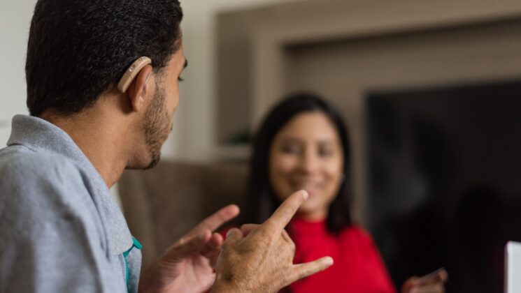 A young man with a hearing aid looking at a woman and using sign language