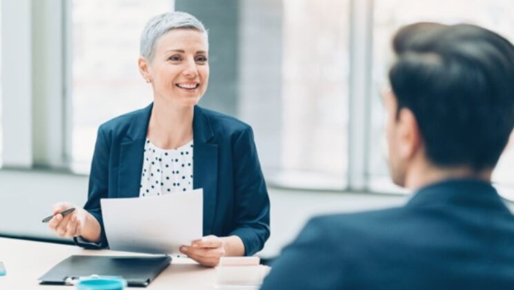 A woman holding papers smiling at a man across a desk