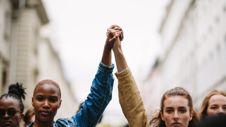 A black and white woman with their arms up and hands clasped together