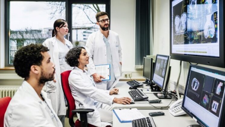 Four people wearing white coats looking at images on screens